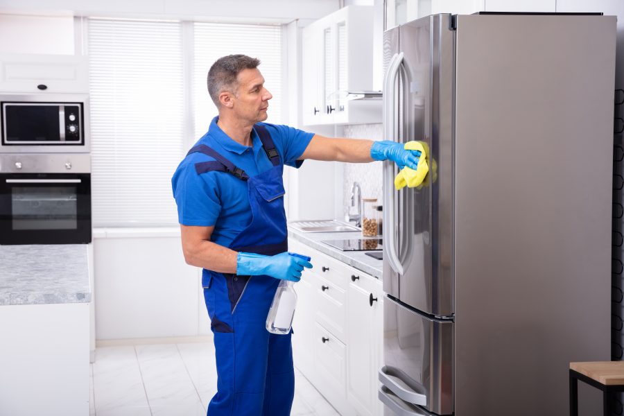 Male Janitor Cleaning Refrigerator With Napkin Male Janitor Cleaning Refrigerator With Yellow Napkin And Spray Detergent